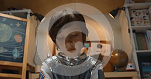 Portrait of happy creative 5-7 little boy in space suit playing with little piece of silver tin foil. Dreaming of future