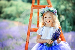 Portrait of happy cute little blonde curly girl wearing lavender dress and wreath and holding bouquet of lavender in lavender