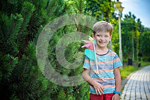 Portrait of a happy cute little boy holding pinwheel at the park. kid hold in hand play with windmill. boy smiling in spring or