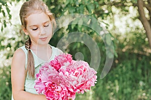 Portrait of a happy cute little caucasian seven year old kid girl, holds in hands and love to see a bouquet of pink peony flowers