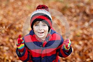 Portrait of happy cute little kid boy with autumn leaves background in colorful clothing. Funny child having fun in fall