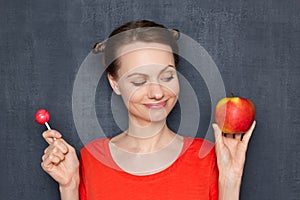 Portrait of happy cute woman holding apple and lollipop in hands