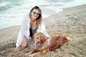 Portrait of happy cute young woman sitting and hugging her dog on the beach