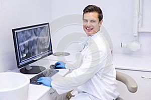 Portrait of happy dentist examining x-ray report on computer