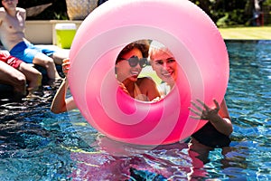 Portrait of happy diverse female friends having pool party, holding swim ring and smiling in garden