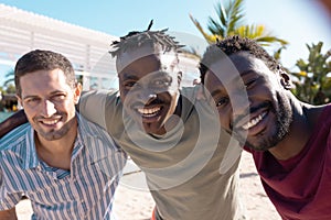 Portrait of happy diverse male friends embracing and smiling at beach, with copy space