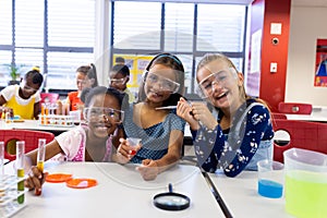 Portrait of happy diverse schoolgirls with chemistry items and liquids in elementary school class