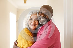 Portrait of happy diverse senior couple embracing and smiling to camera at home