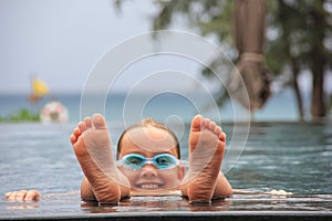 Portrait of happy eight year old boy having fun in swimming infinity pool in summer vacation.
