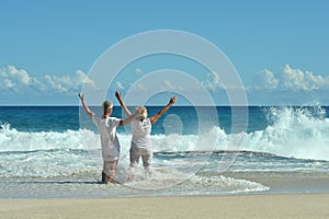 Portrait of happy elderly couple resting on beach waving hands