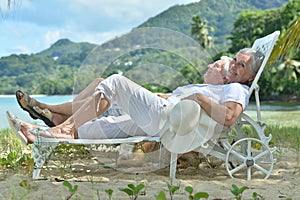 Portrait of happy elderly couple resting in chaise lounges at tropical beach