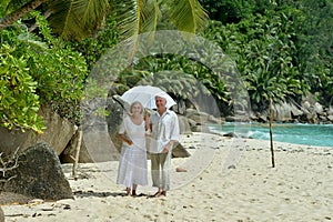 Portrait of happy elderly couple resting on tropical beach with umbrella