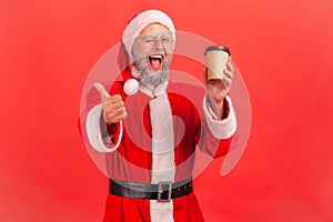 Portrait of happy elderly man with gray beard wearing santa claus costume standing with disposable