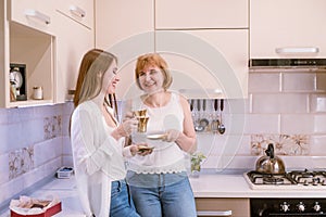 Portrait of a happy elderly mother and daughter in modern light kitchen interior