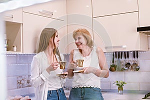 Portrait of a happy elderly mother and daughter in modern light kitchen interior laughing and looking on each other