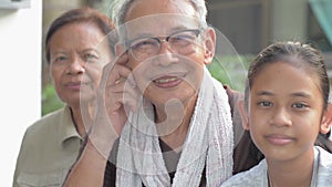 Portrait of happy elderly retirement grandparents with adorable granddaughter sitting together and smiling while looking at camera