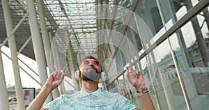 Portrait of the happy emotional african man in luxury pink sunglasses listening to music in headphones and raising hands