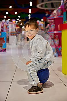 Portrait of happy excited boy child sitting on ball during shopping in mall