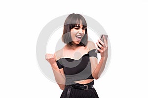 Portrait of a happy excited girl holding mobile phone and celebrating win isolated over grey background