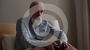 Portrait of happy excited gray-haired mature male winning on video console game using gamepad at home.