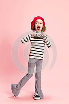 Portrait of happy, excited little girl, cild in striped sweater and red beret posing with vintage photo camra agaisnt