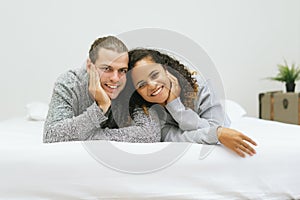 Portrait of happy excited mixed-race young couple lying on bed her smile together and looking at camera at home during the