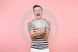 Portrait of happy excited young man in striped t-shirt holding bundle lots of dollars, cash money, ardor gesture on copy