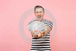 Portrait of happy excited young man in striped t-shirt holding bundle lots of dollars, cash money, ardor gesture on copy