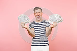 Portrait of happy excited young man in striped t-shirt holding bundle lots of dollars, cash money, ardor gesture on copy