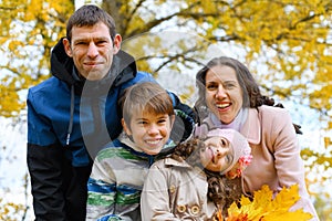 Portrait of a happy family in an autumn park. People pose against the background of beautiful yellow trees. They hug and are happy