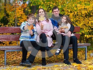 Portrait of a happy family in an autumn park. People sitting on a bench. Posing against the background of beautiful yellow trees.