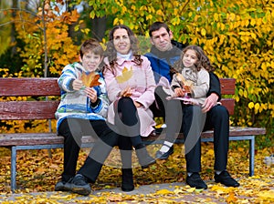 Portrait of a happy family in an autumn park. People sitting on a bench. Posing against the background of beautiful yellow trees.