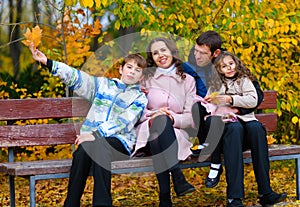 Portrait of a happy family in an autumn park. People sitting on a bench. Posing against the background of beautiful yellow trees.