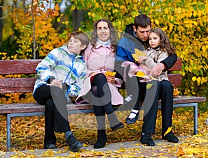 Portrait of a happy family in an autumn park. People sitting on a bench. Posing against the background of beautiful yellow trees.