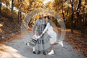 Portrait of happy family on background of golden park in autumn day. Father, daughter and pregnant mother.