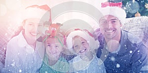 Composite image of portrait of a happy family with christmas hats sitting on the sofa