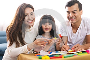 Portrait of happy family daughter girl is learning to use colorful play dough blocks toy together with parent.