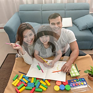 Portrait of happy family daughter and parent drawing and reading together.