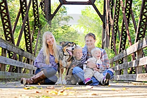 Portrait of Happy Family and Dog Sitting On Bridge in Autumn Woo