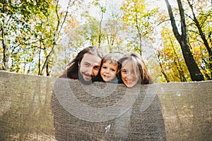 Portrait of happy family hiding behind a soft fabric fence in autumn park