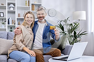 Portrait of happy family at home, adult mature couple man and woman sitting on sofa in living room and looking