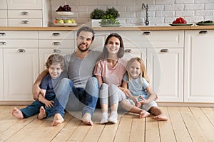 Portrait happy family hugging, sitting on warm floor in kitchen