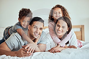 Portrait of happy family with little kids lying on the bed at home. Smiling couple bonding with their son and daughter
