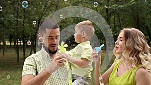 Portrait of a happy family with a little son in Park with soap bubbles. Slow mo.
