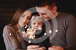 Portrait of happy family, mom, dad and baby girl with sparklers and light. family in anticipation of Christmas. selective photo