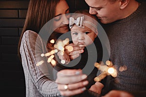 Portrait of happy family, mom, dad and baby girl with sparklers and light. family in anticipation of Christmas. selective photo