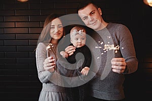 Portrait of happy family, mom, dad and baby girl with sparklers and light. family in anticipation of Christmas. selective photo