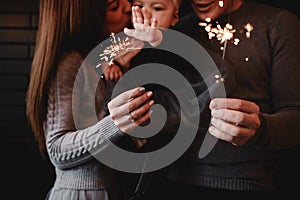 Portrait of happy family, mom, dad and baby girl with sparklers and light. family in anticipation of Christmas. selective photo