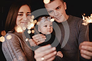 Portrait of happy family, mom, dad and baby girl with sparklers and light. family in anticipation of Christmas. selective photo