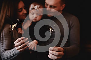 Portrait of happy family, mom, dad and baby girl with sparklers and light. family in anticipation of Christmas. selective photo